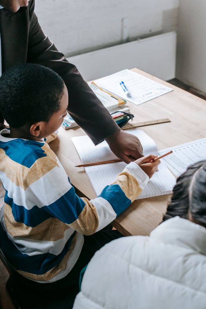 services-img Crop black female helping ethnic boy and girl with assignment while studying in school classroom