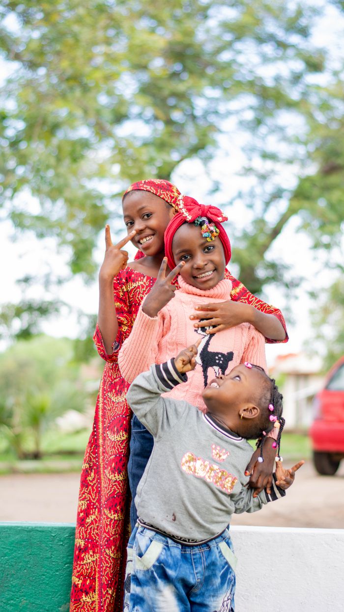 Three happy children dressed in vibrant clothes posing playfully outdoors, exuding joy and friendship.