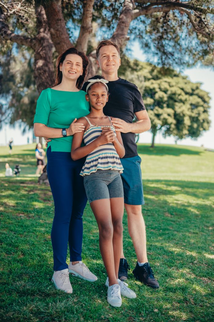 Smiling family standing together in a sunny park, symbolizing happiness and togetherness.